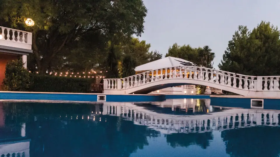 Pileta con puente iluminado al atardecer · Punto Aparte Multi Espacio